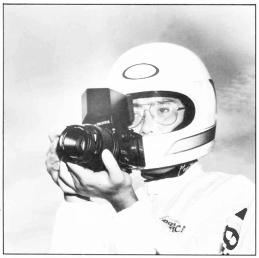 A man wearing glasses and a motorsports helmet uses the Bronica Action Prism Finder-E to compose a photograph on a Bronica ETRS Mk-II camera.